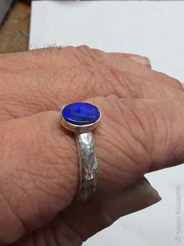 A silver ring with a hammered texture around the band. A blue opal cabochon is mounted on it